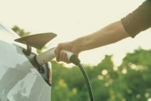 Man recharging battery for electric car during autumnal road trip