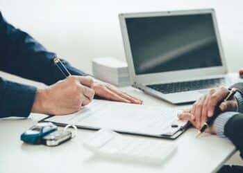 An image of two people signing a contract with a car key and toy car on the desk.